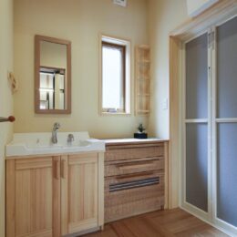 洗面室。サッシ枠、洗面台、洗面収納棚は赤松無垢材。木肌は経年変化により美しい飴色に変化します。床、引出し収納はタモ材を使用。ウェーブを施すことで木肌が心地よい肌触りです。