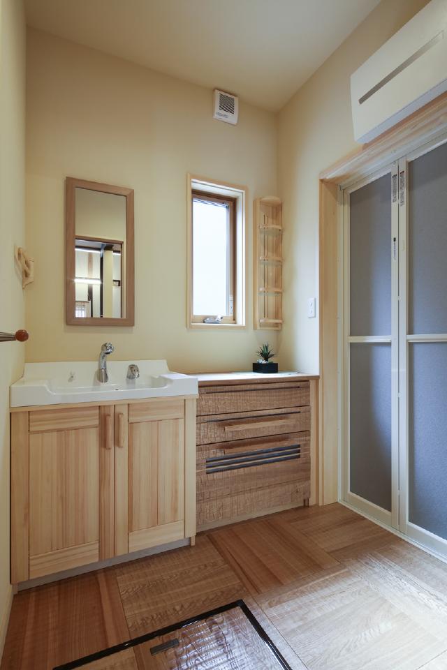 洗面室。サッシ枠、洗面台、洗面収納棚は赤松無垢材。木肌は経年変化により美しい飴色に変化します。床、引出し収納はタモ材を使用。ウェーブを施すことで木肌が心地よい肌触りです。